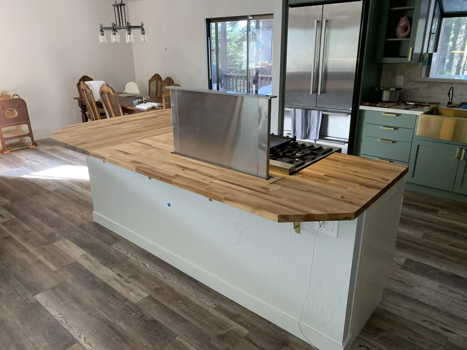 Modern kitchen with a large wooden island, stainless cooktop, and gray cabinets by a window