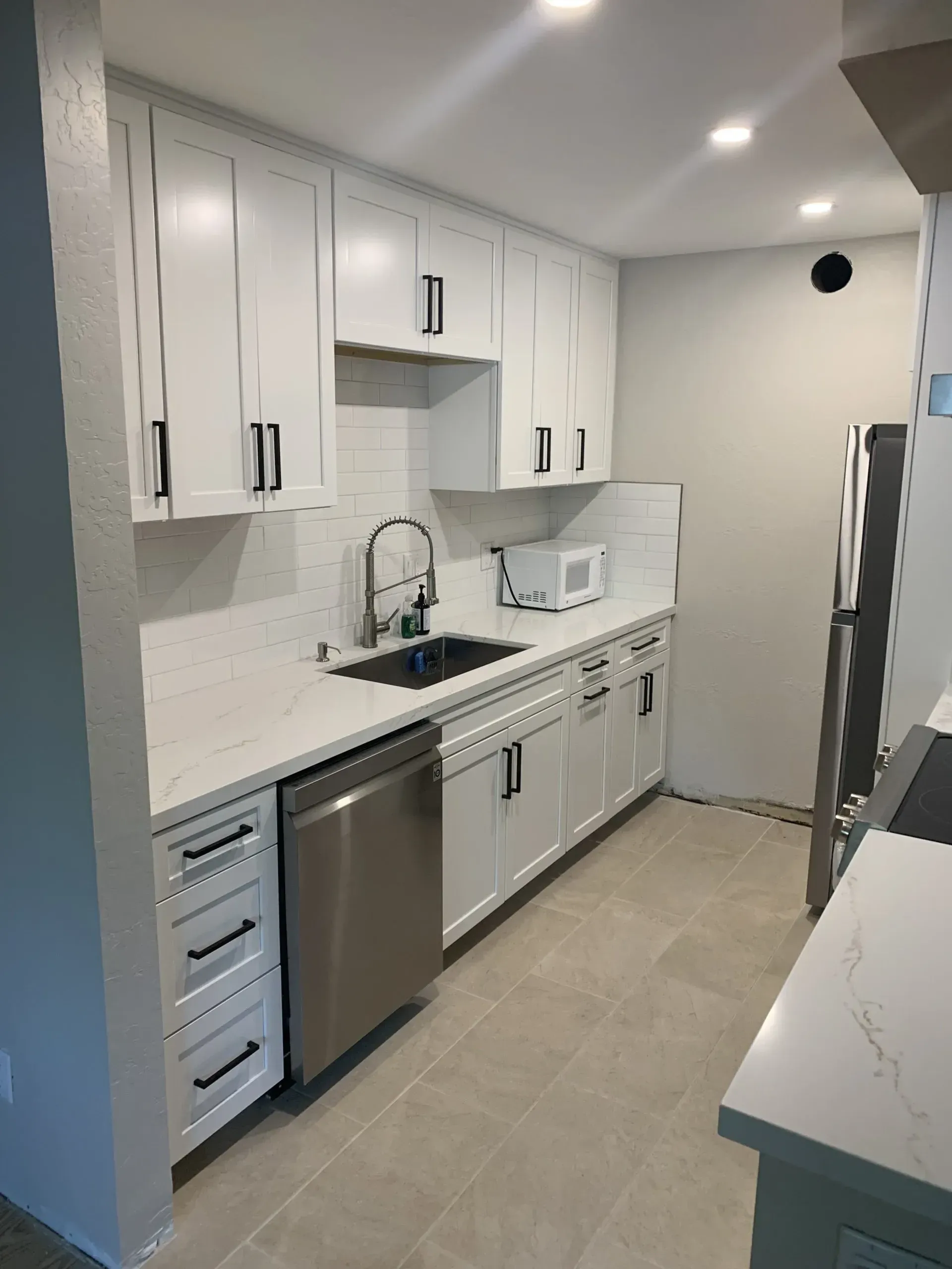 Modern white galley kitchen with stainless steel appliances, dark sink, and marble-look countertops