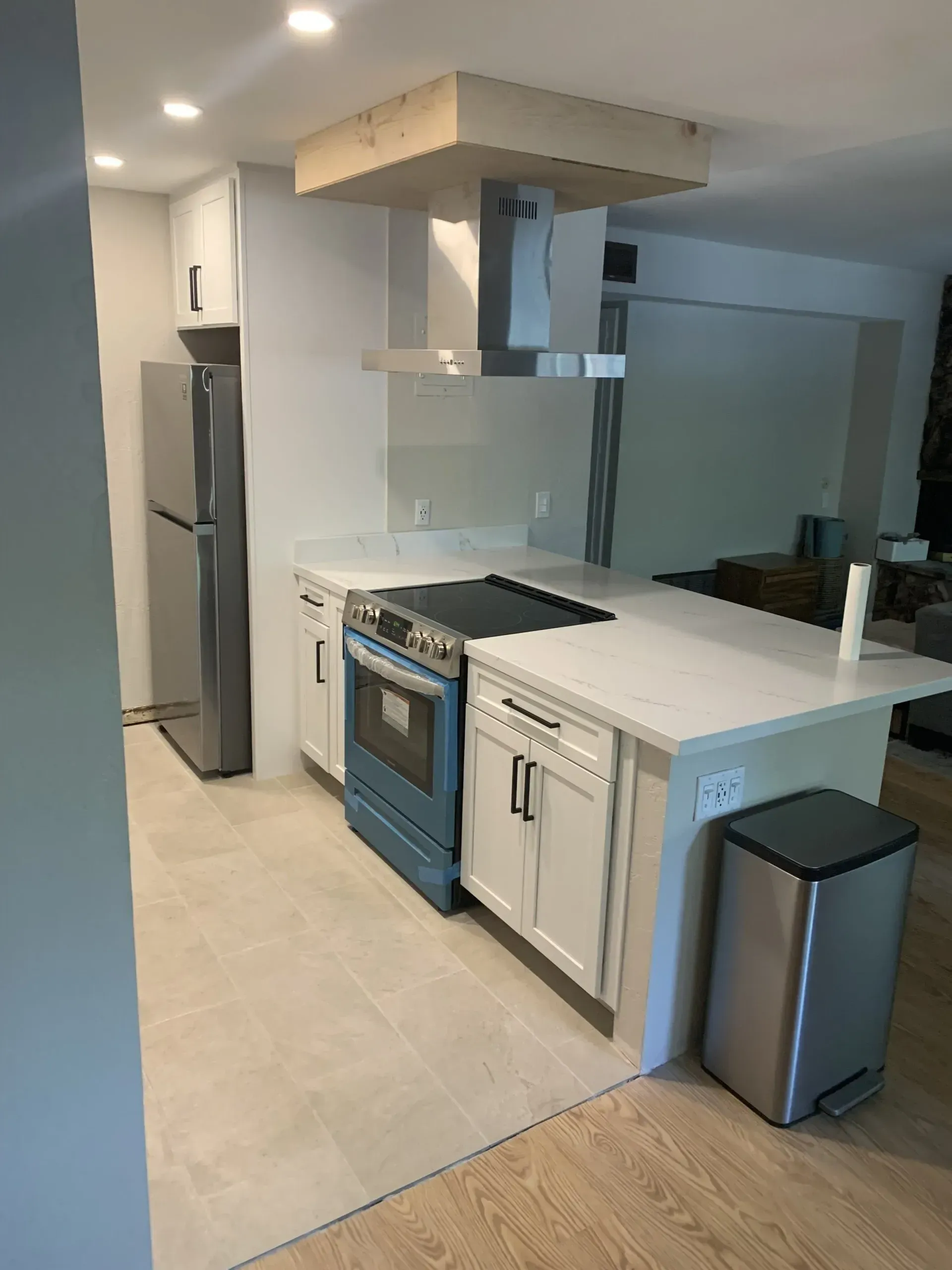 Modern kitchen with island, stove, stainless fridge, sink, and trash bins in a bright open-plan room