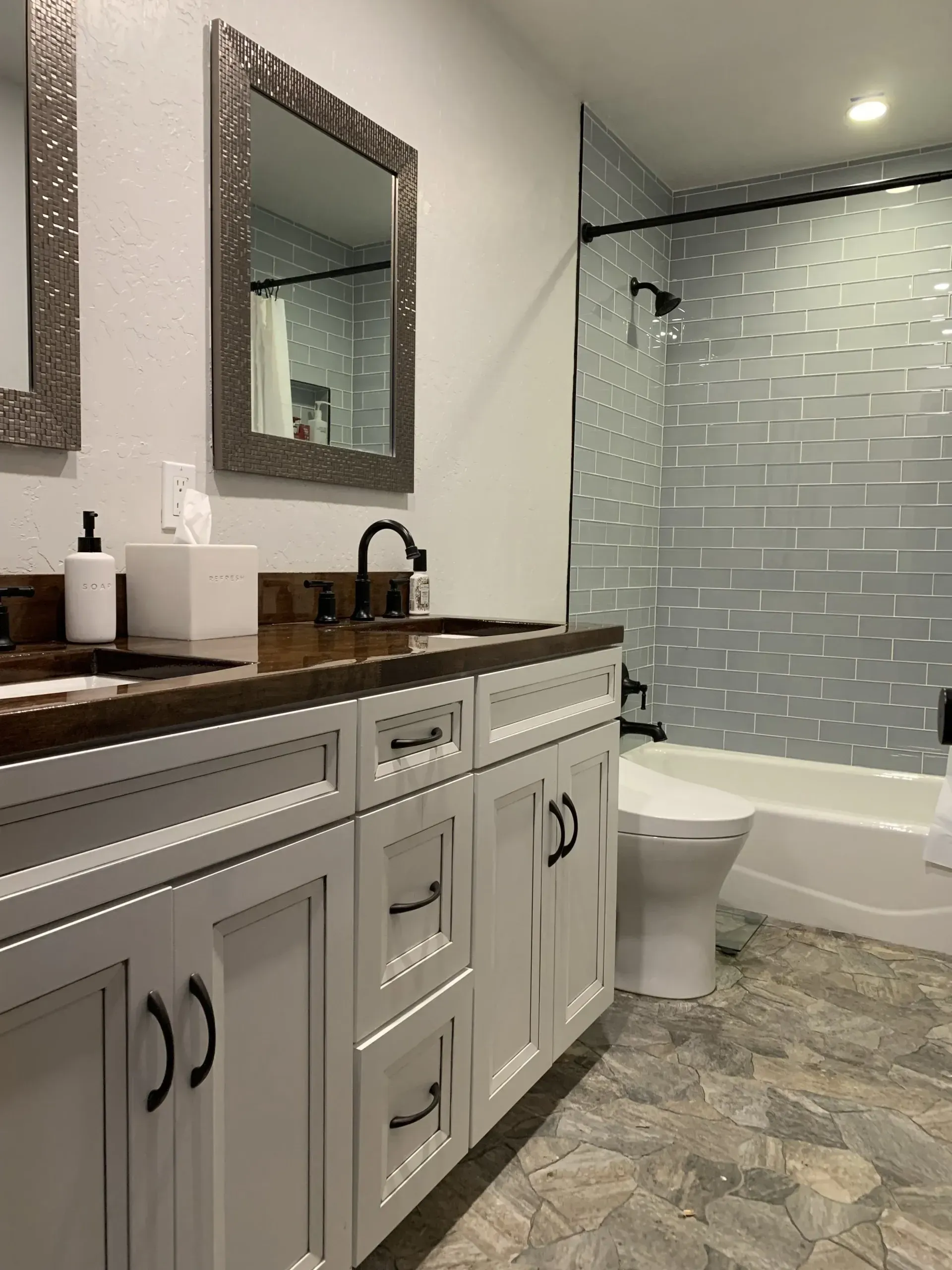 Modern bathroom with white vanity, dark countertop, mirror, and tiled shower-tub area
