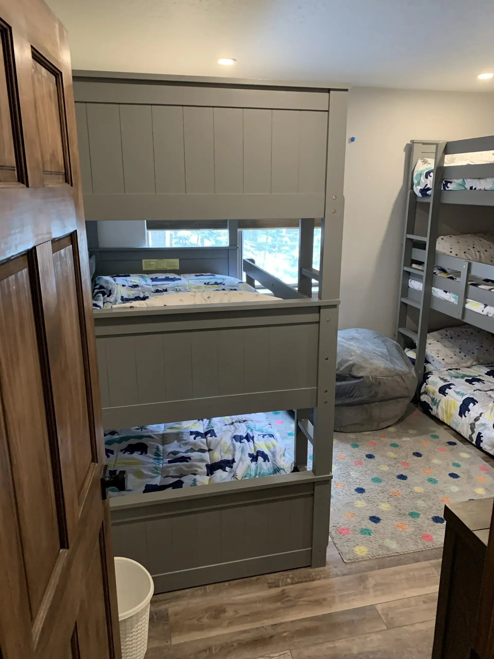 Children’s bedroom with bunk beds, gray dresser, crib, and toy-covered floor