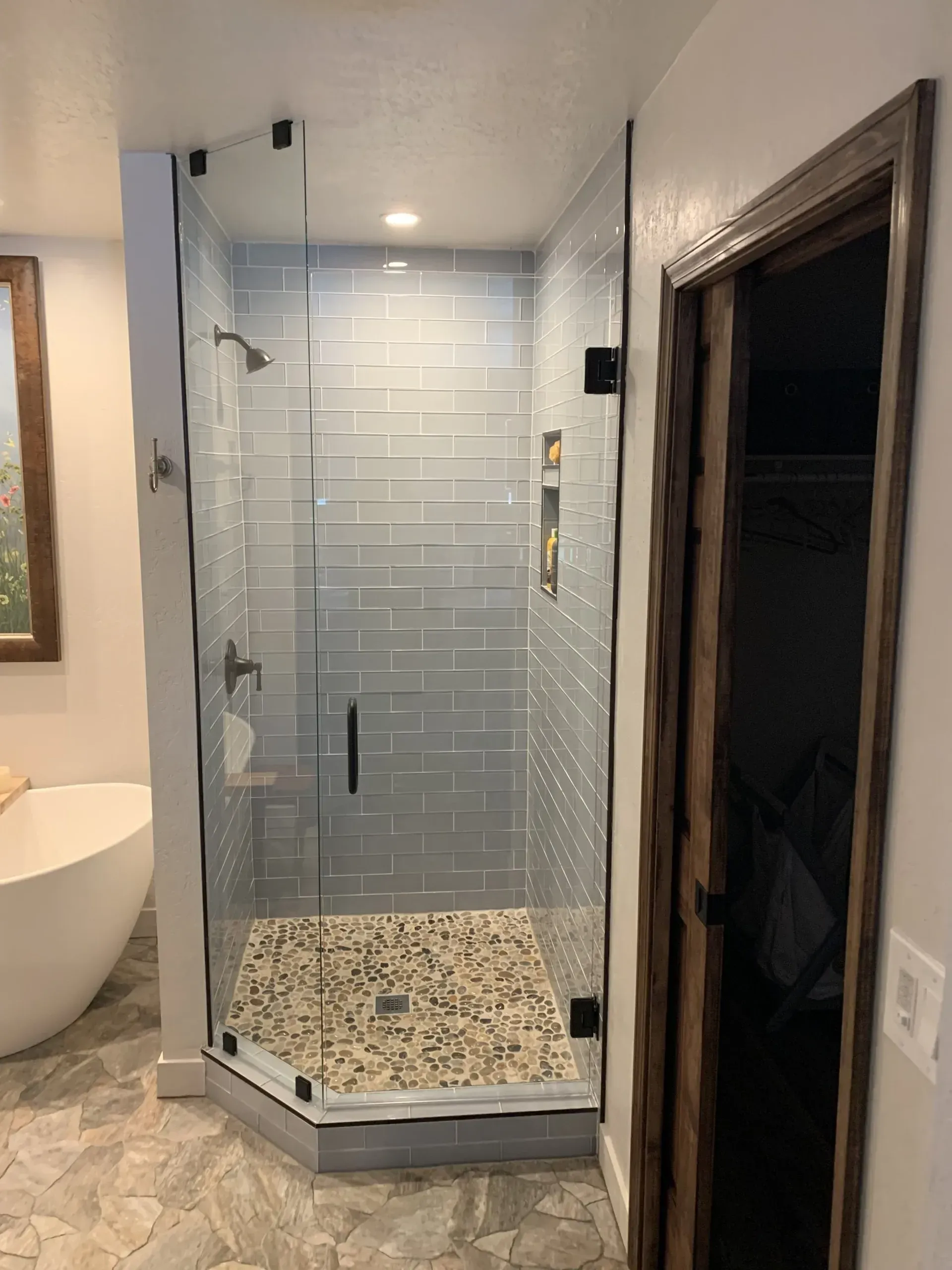 Modern bathroom with glass walk-in shower, mosaic tile floor, and white freestanding tub