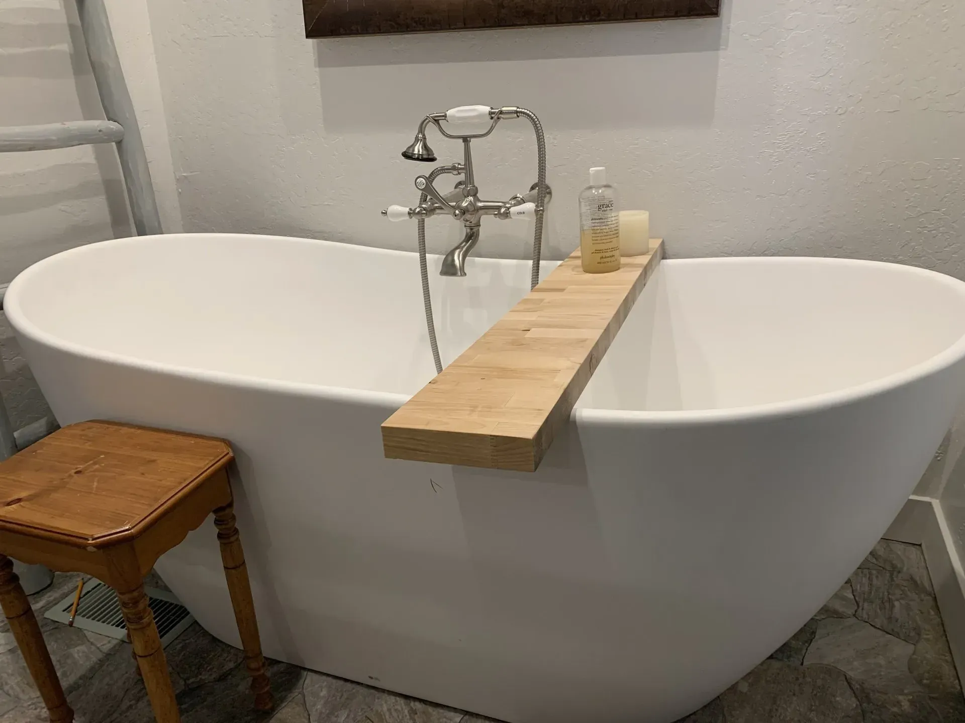 White freestanding bathtub with vintage faucet and wooden bath tray in a tiled bathroom.