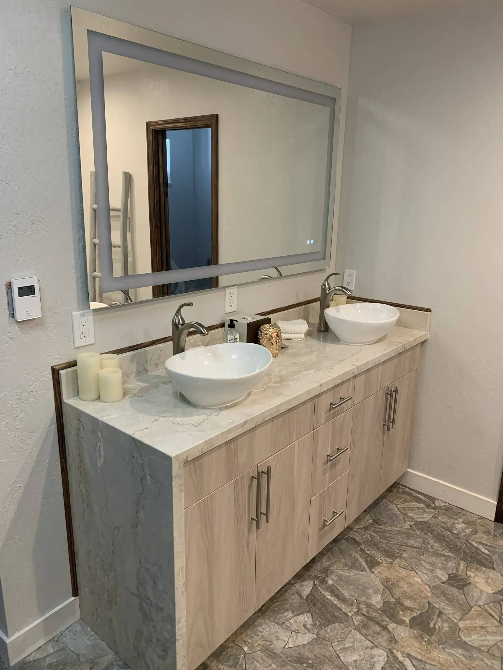 Modern bathroom vanity with two sinks, large mirror, and light wood cabinets against gray walls.