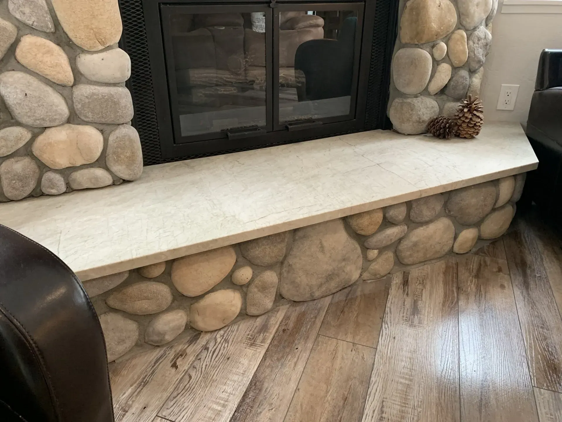 Stone fireplace with black glass doors, white mantel, and a curved stone bench in a room with wood flooring