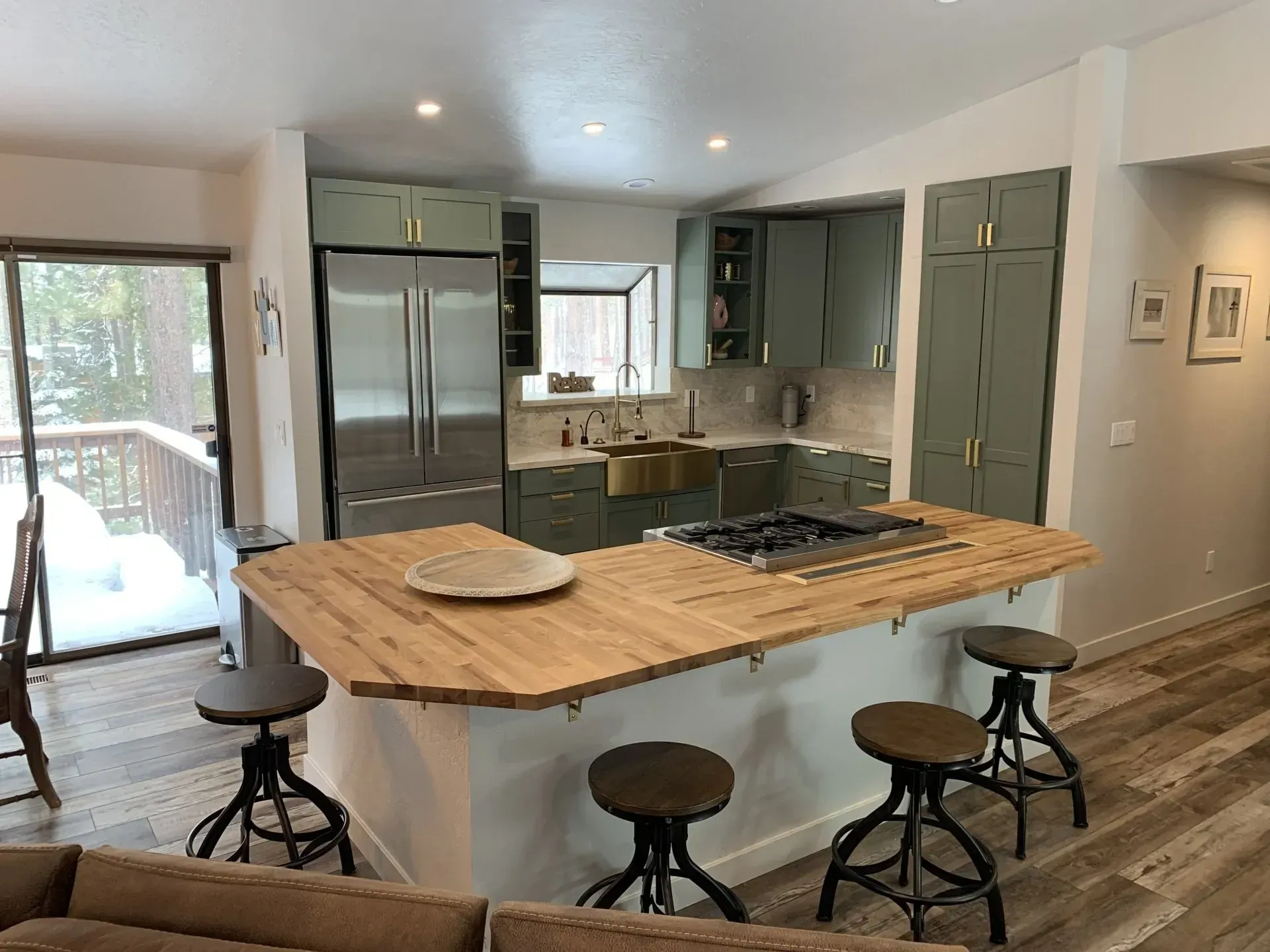 Modern kitchen with wood island, stools, stainless fridge, and sliding glass door to deck