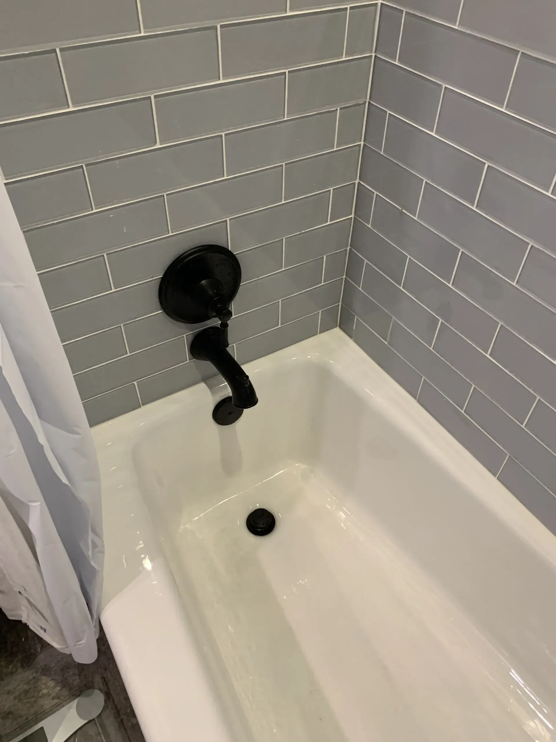 Bathtub with gray tiled wall and black shower head on the left side of the tub.