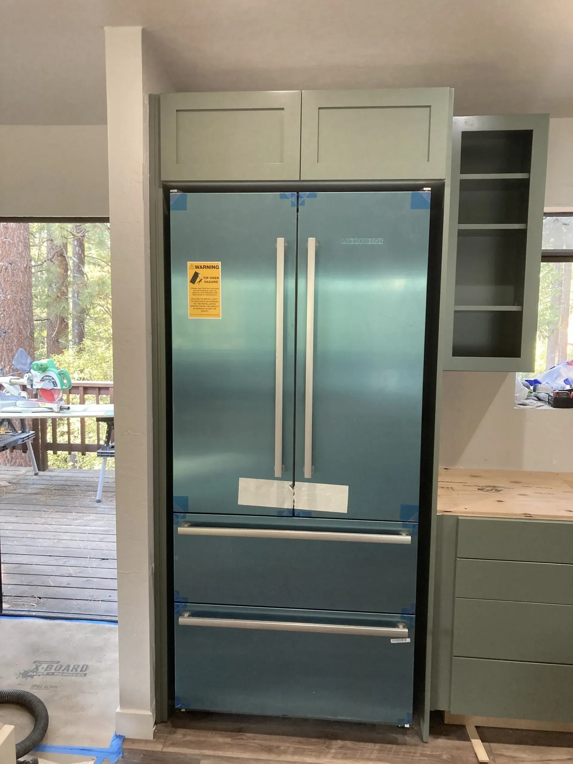 Blue French-door refrigerator in a modern kitchen, next to open shelving and a patio doorway.
