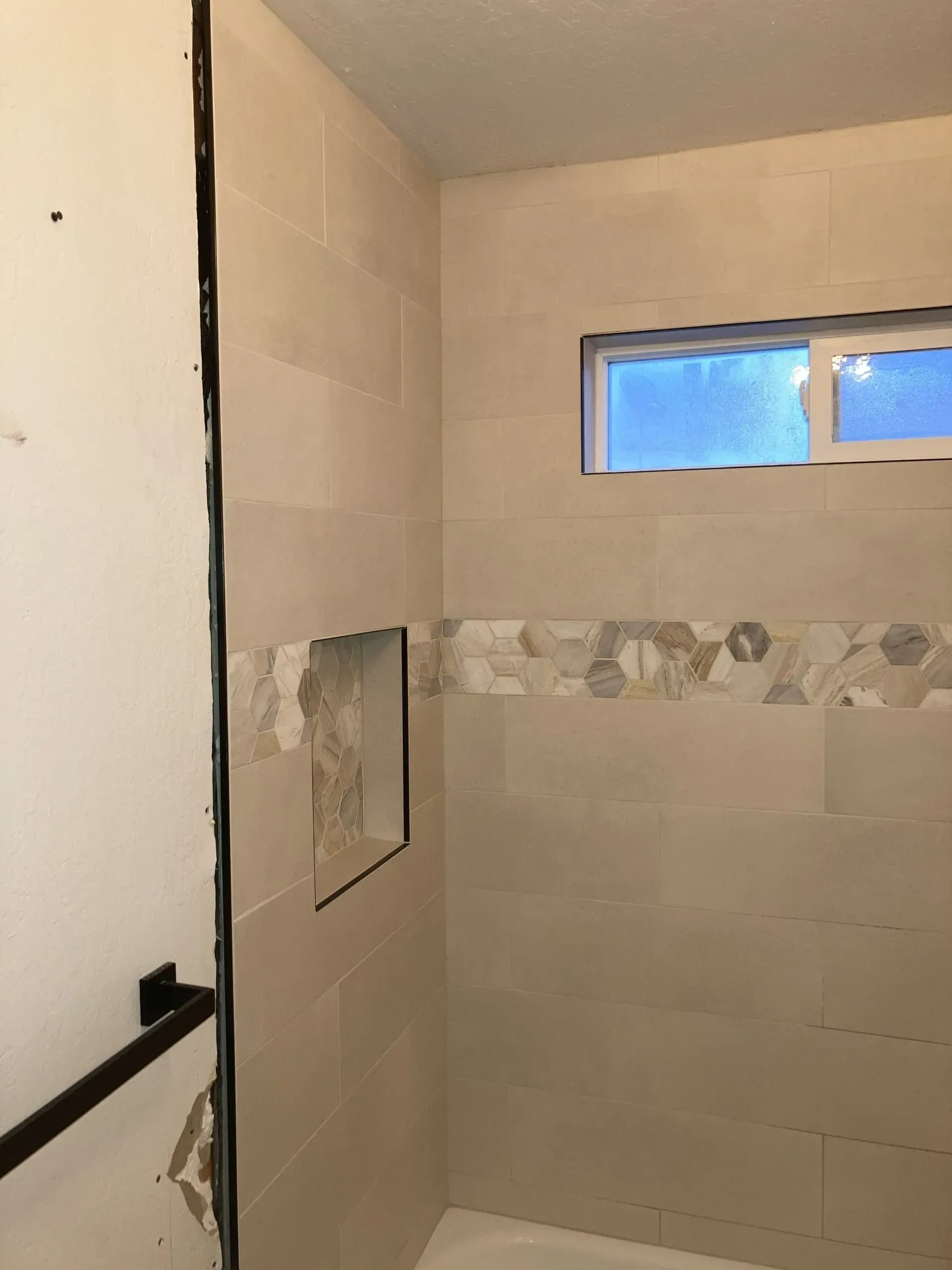 Bathroom shower under construction with tiled walls, a window, and a recessed niche.