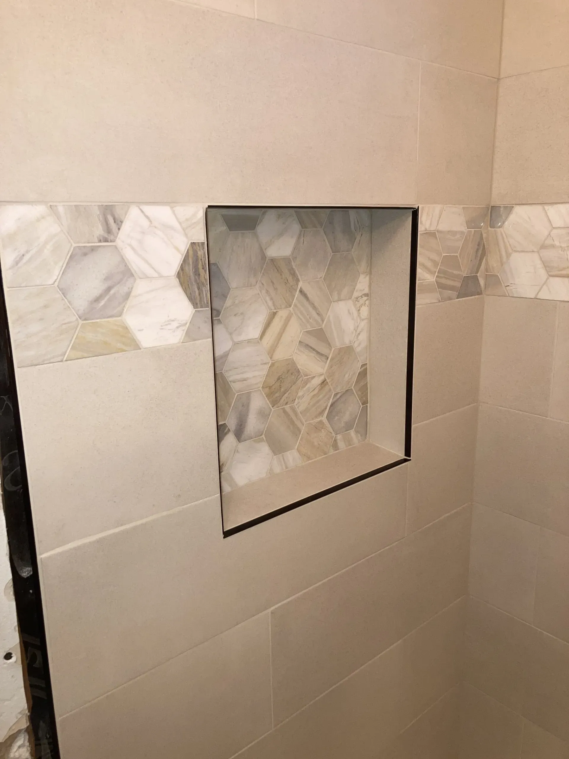 Tiled shower wall with a recessed niche lined in stone-pattern mosaic tiles