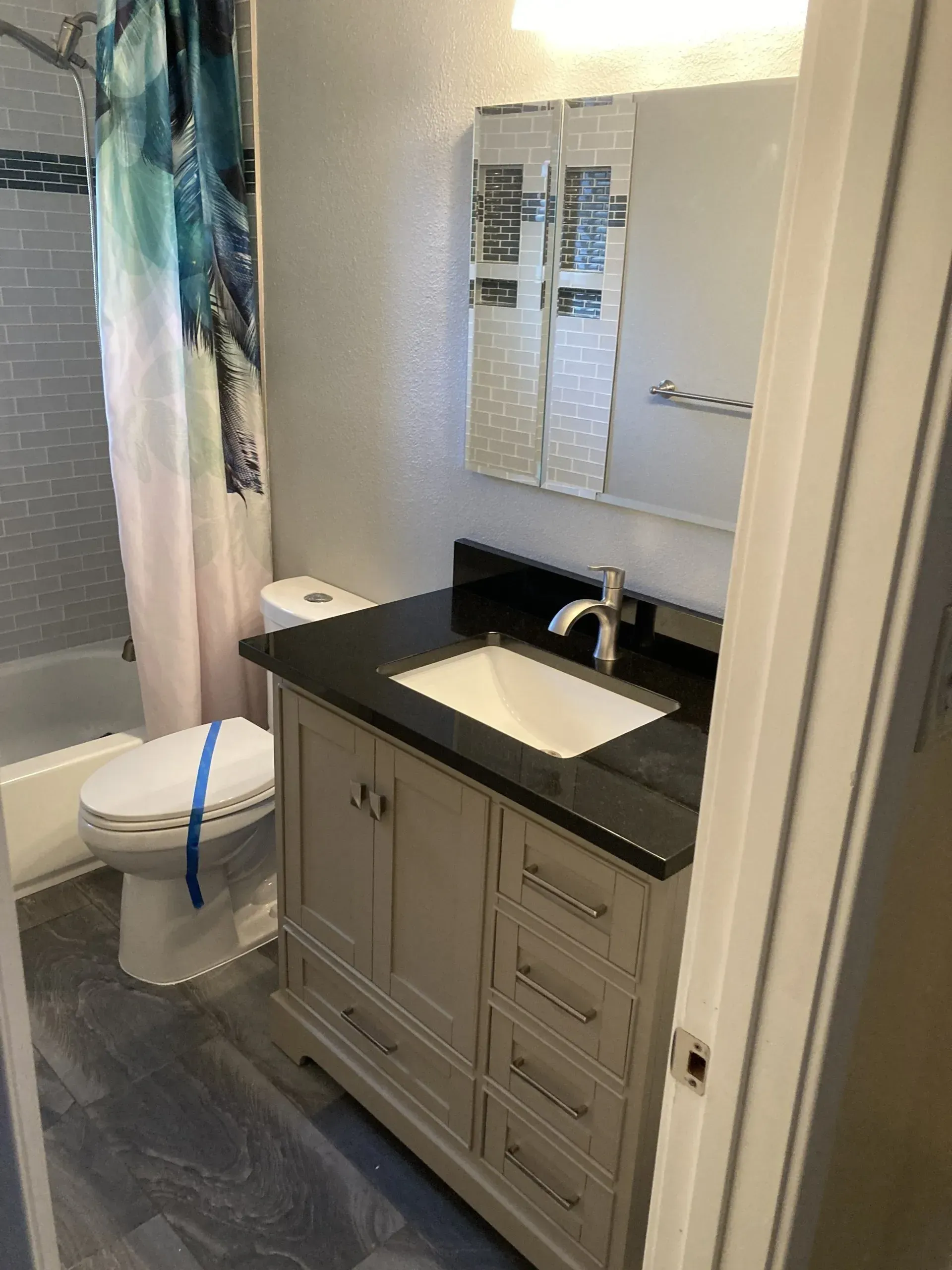Small bathroom vanity with black countertop, white sink, mirror, and toilet beside a striped shower curtain.