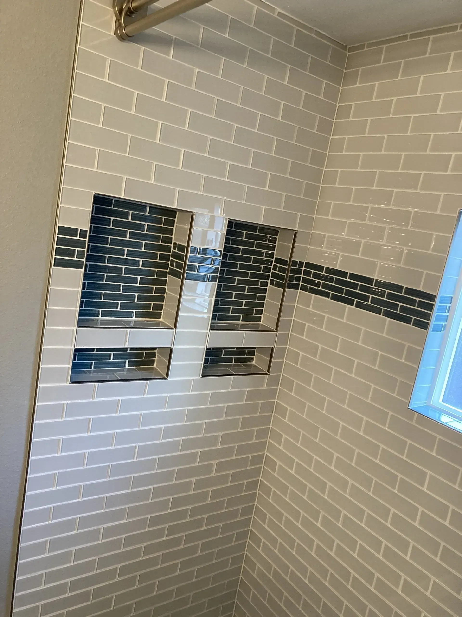 White tiled shower corner with two wall-mounted shower caddies and a small window.