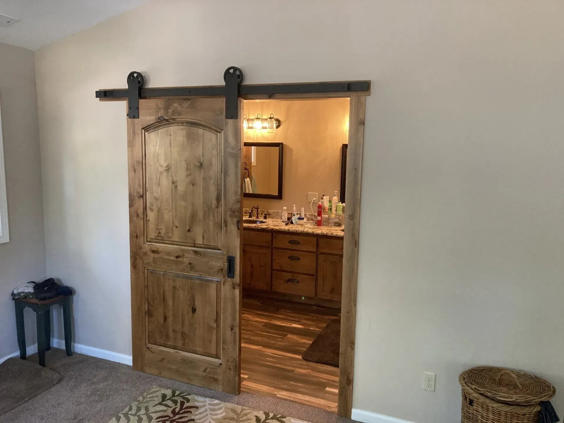 Rustic sliding barn door opening to a warmly lit bathroom with wooden vanity and mirror