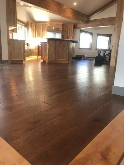 Empty living room with hardwood floors, vaulted ceiling, and large windows letting in warm sunlight