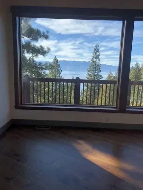 Empty room with dark floor, large window, and view of trees, lake, and mountains.