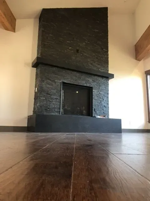 Empty modern room with a large dark stone fireplace and wooden floorboards