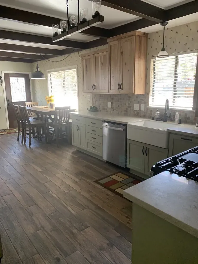 Modern kitchen with wood floors, light wood cabinets, and a dining table by a window.