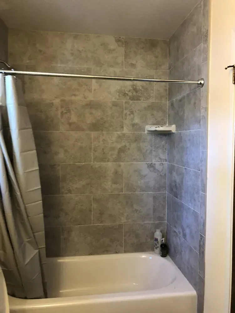 Small tiled bathroom with a bathtub, shower rod, curtain, and wall shelf.