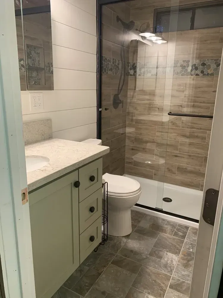 Small modern bathroom with vanity, toilet, tiled floor, and glass walk-in shower.