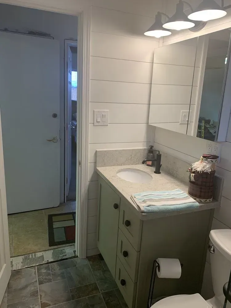 Bathroom vanity with round sink, mirror, towel, and toilet paper holder beside a doorway.