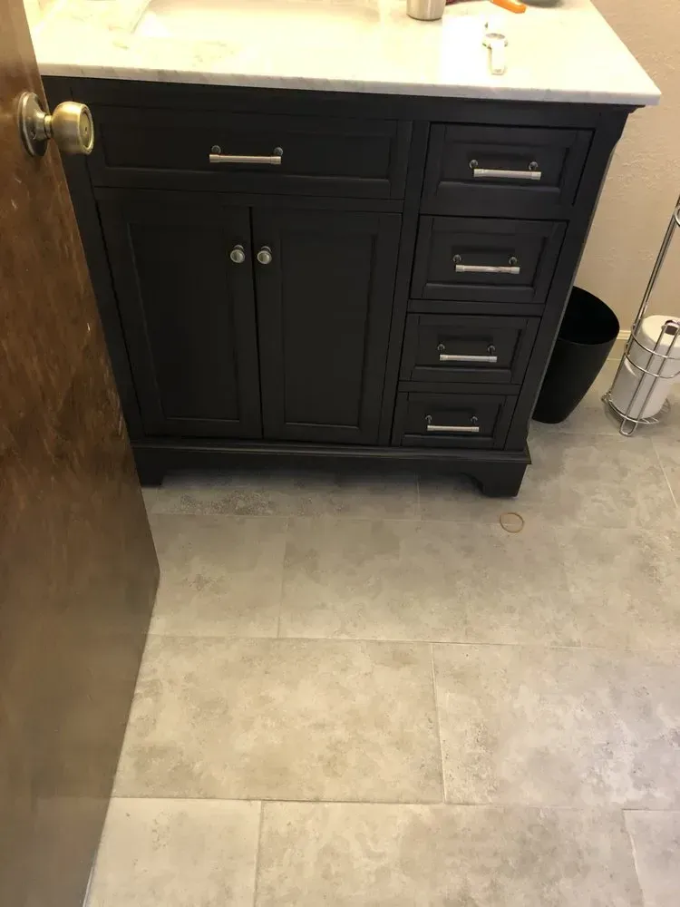 Black bathroom vanity with white countertop and beige tile floor next to a door