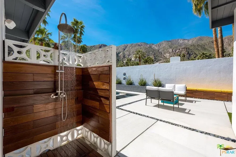 Outdoor patio with a wood-paneled shower, white walls, and lounge chairs under a sunny mountain view