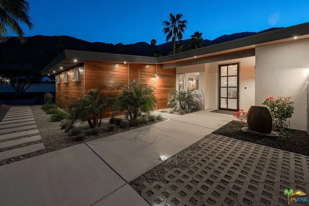 Modern house exterior at dusk with warm porch lights, landscaped walkway, and desert-style plants