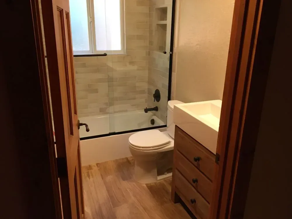 Small bathroom with a bathtub, toilet, wood floor, and vanity sink.