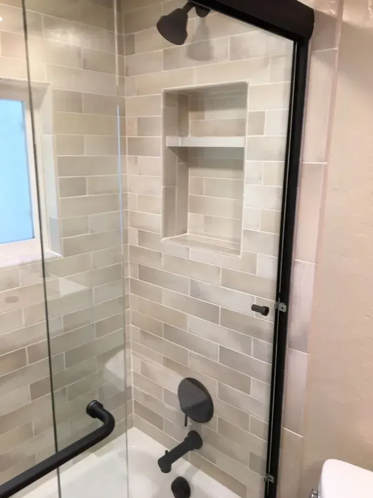 Modern tiled shower with black grab bars, built-in shelf, and handheld showerhead.