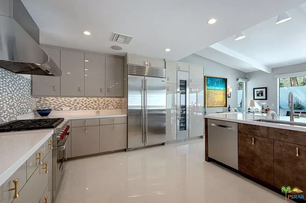 Modern kitchen with stainless steel appliances, white counters, and glossy tile flooring.