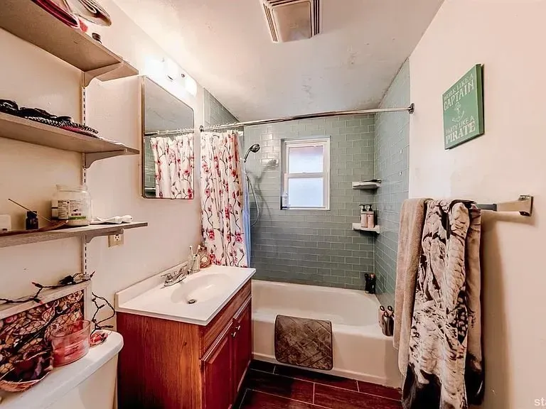 Small bathroom with bathtub, sink vanity, shower curtain, shelves, and towels on the wall.