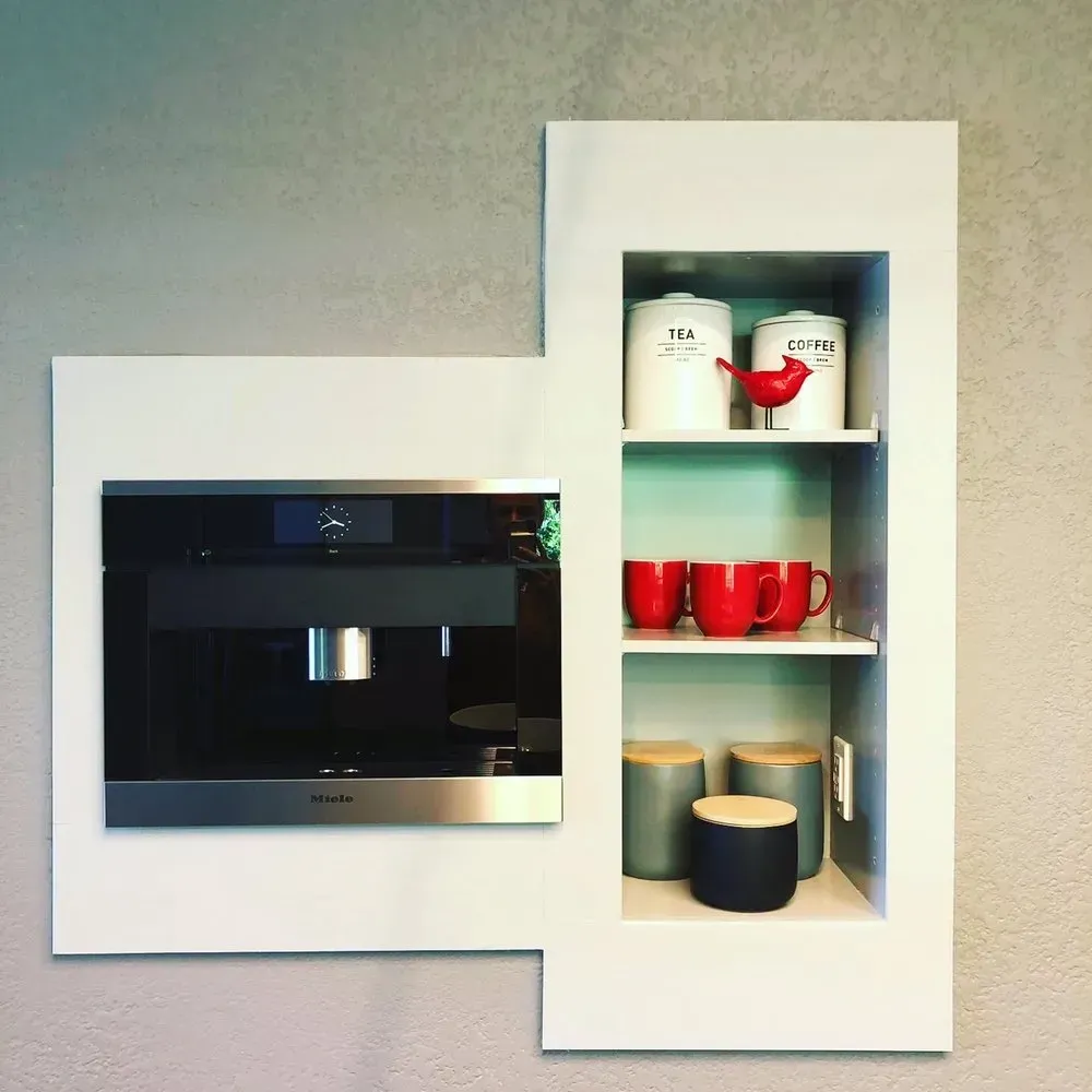Built-in black oven beside white cabinet with red and white mugs displayed on shelves
