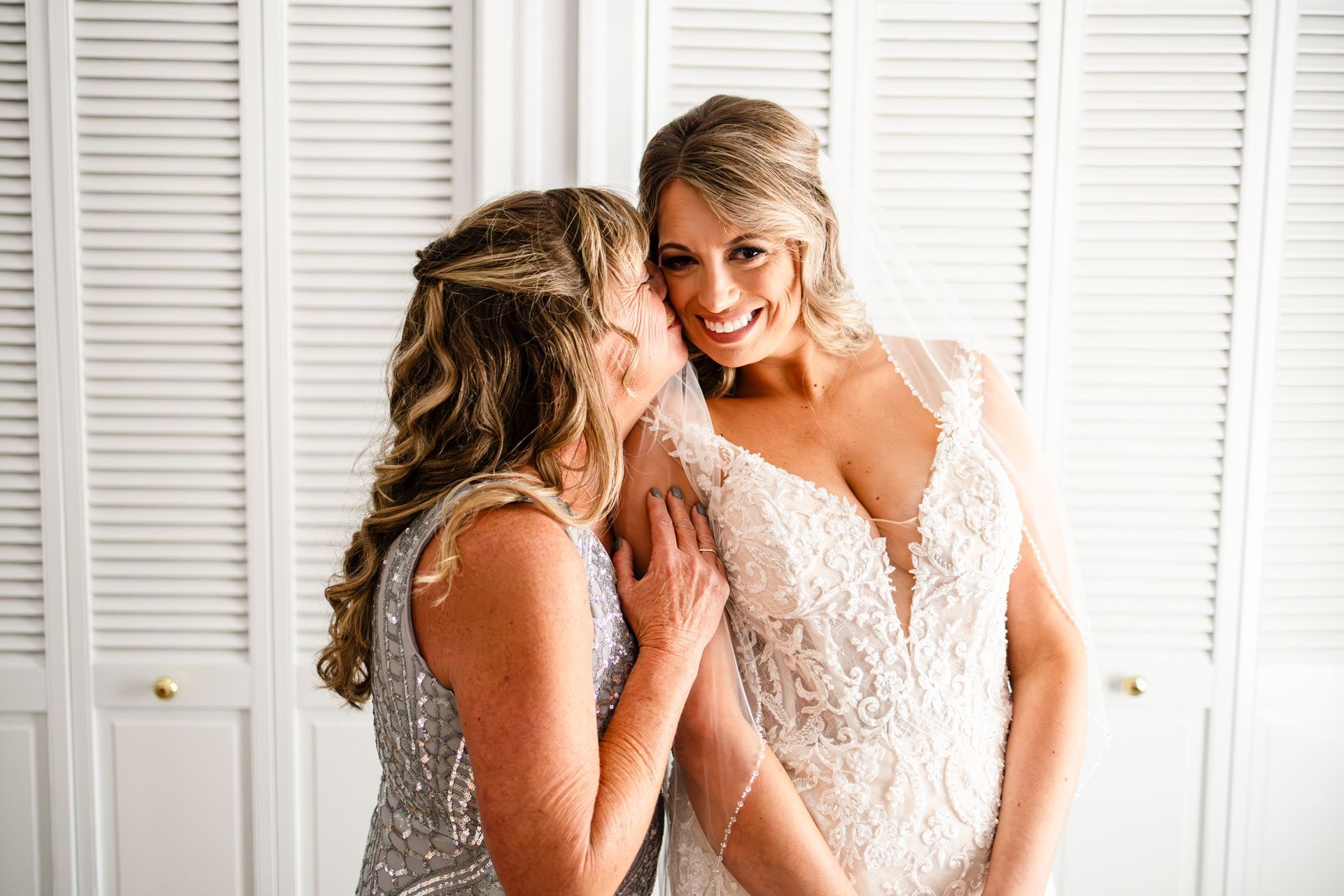 A woman is kissing another woman on the cheek while getting ready for her wedding taken by Ever After Studio.