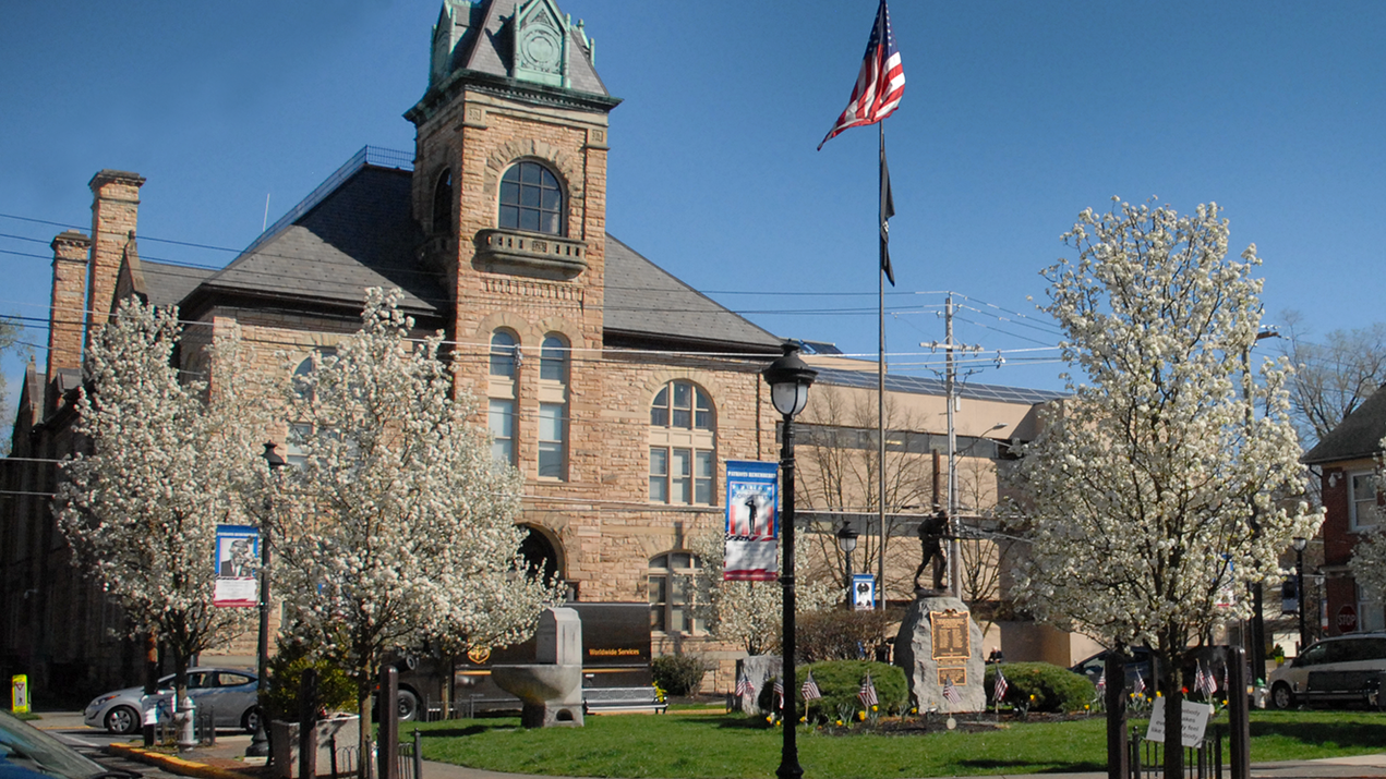 A large stone building with a clock tower and a flag flying in front of it in Stroudsburg