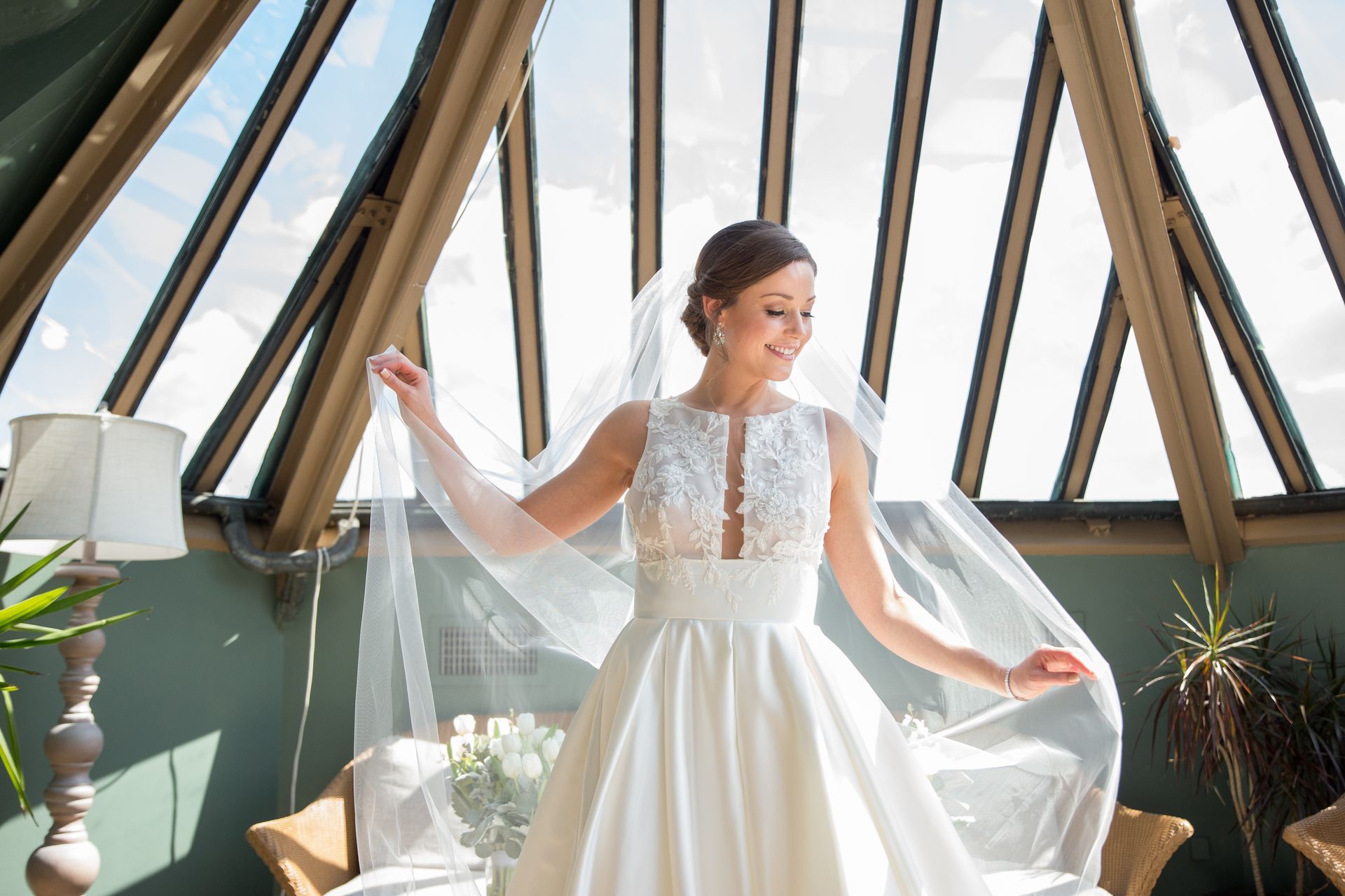 A bride in a wedding dress and veil is standing in front of a window taken by Ever After Studio.
