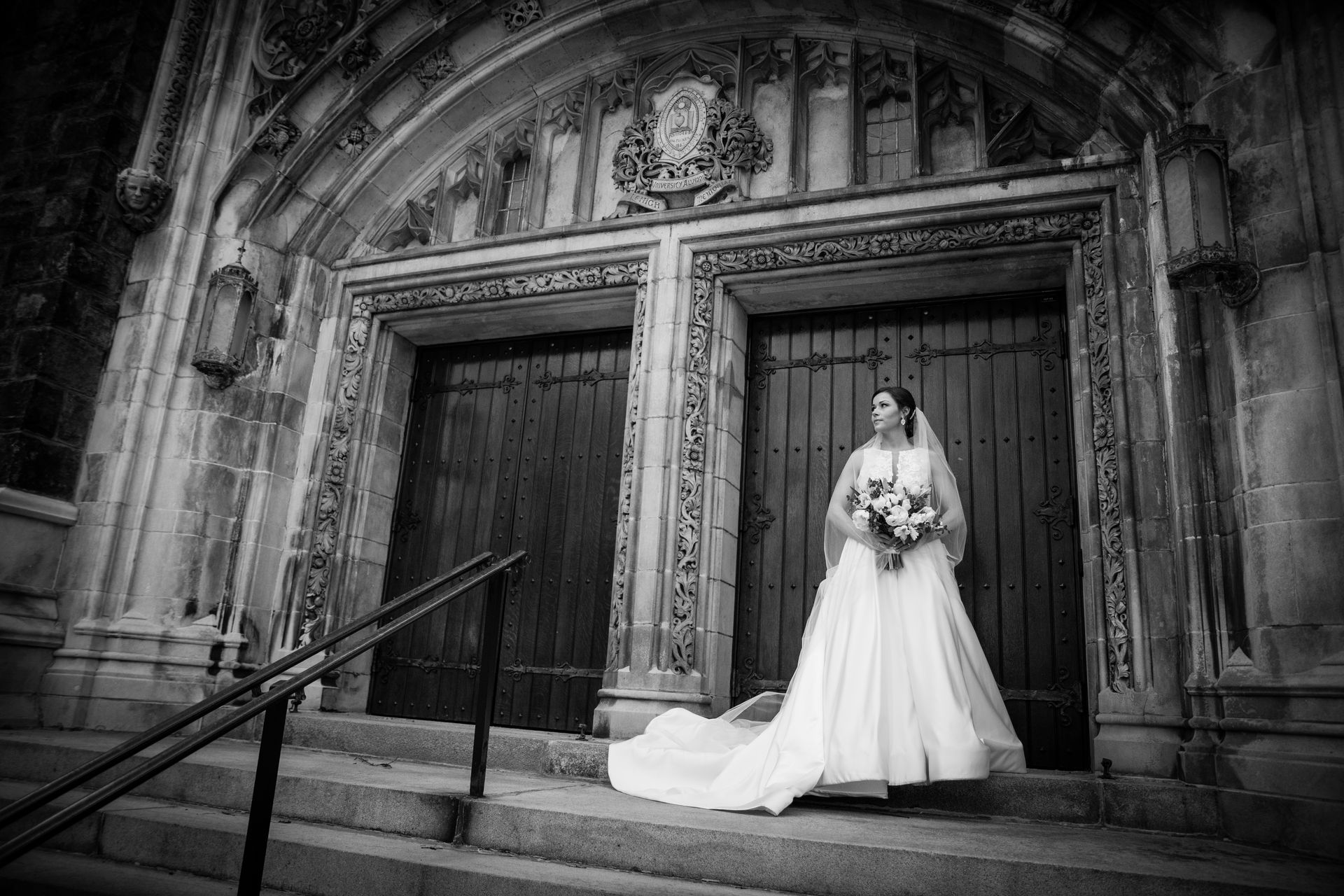 A black and white photo of a bride in a wedding dress standing on the steps of a church taken by Ever After Studio.
