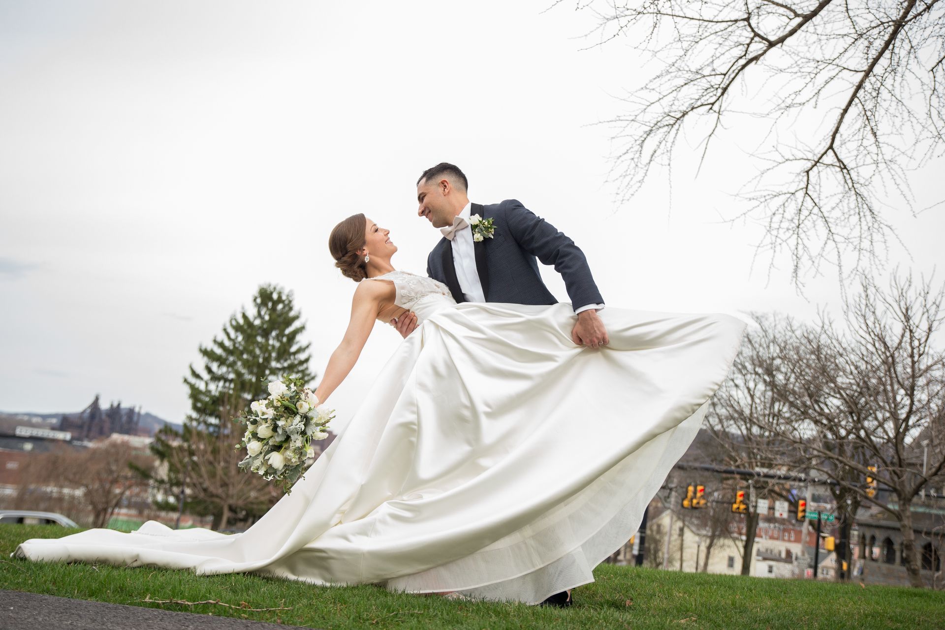 A bride and groom are posing for a picture while the bride 's dress is blowing in the wind taken by Ever After Studio.