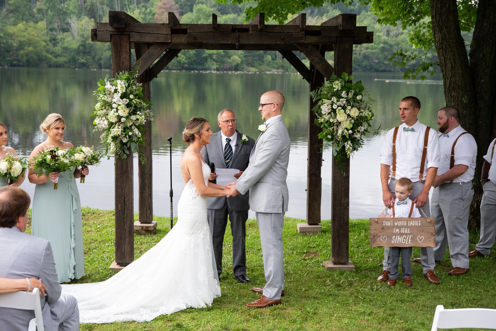 A bride and groom are holding hands during their wedding ceremony in front of a lake taken by Ever After Studio.