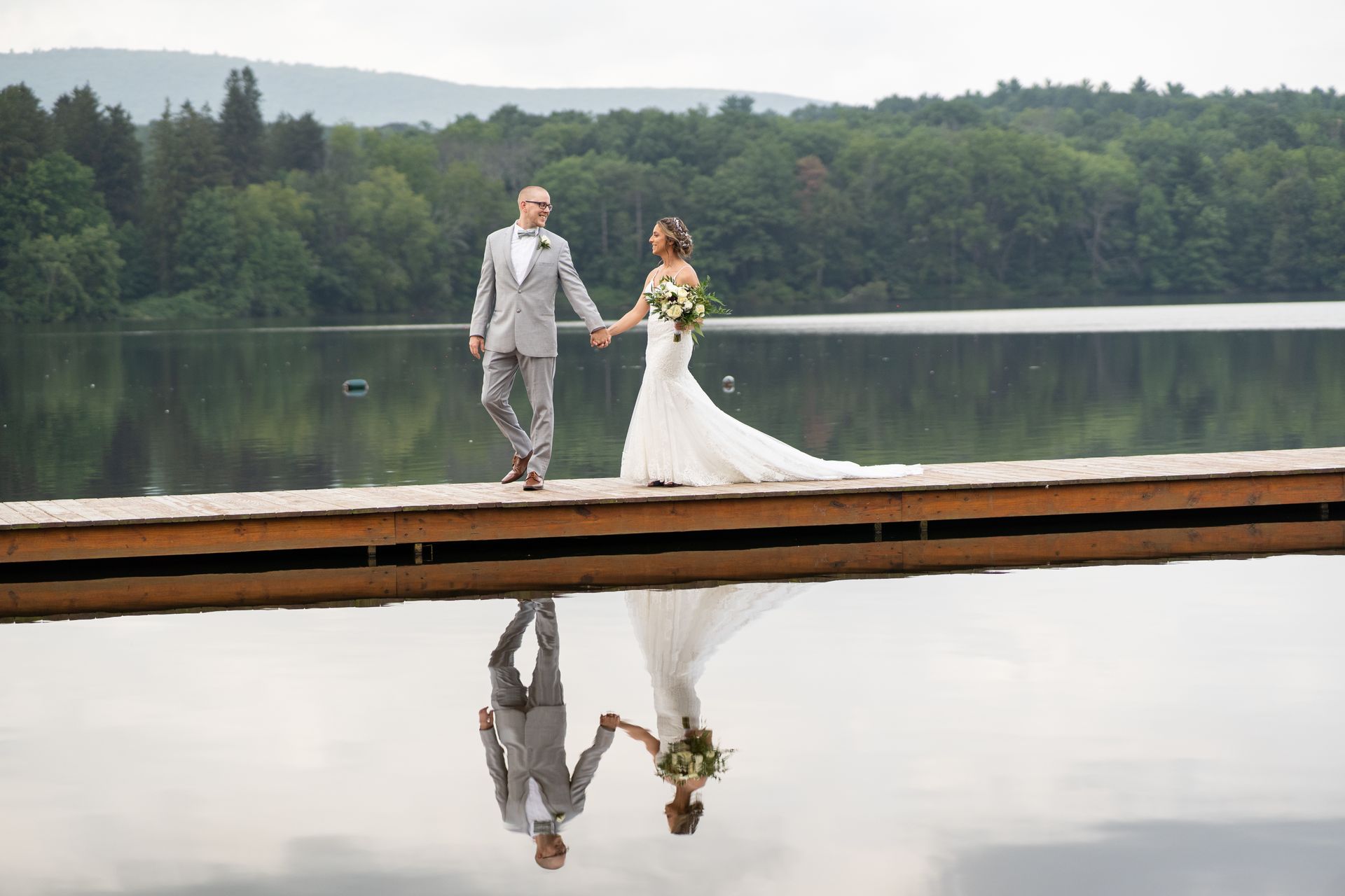 A bride and groom are walking on a dock overlooking a lake taken by Ever After Studio.