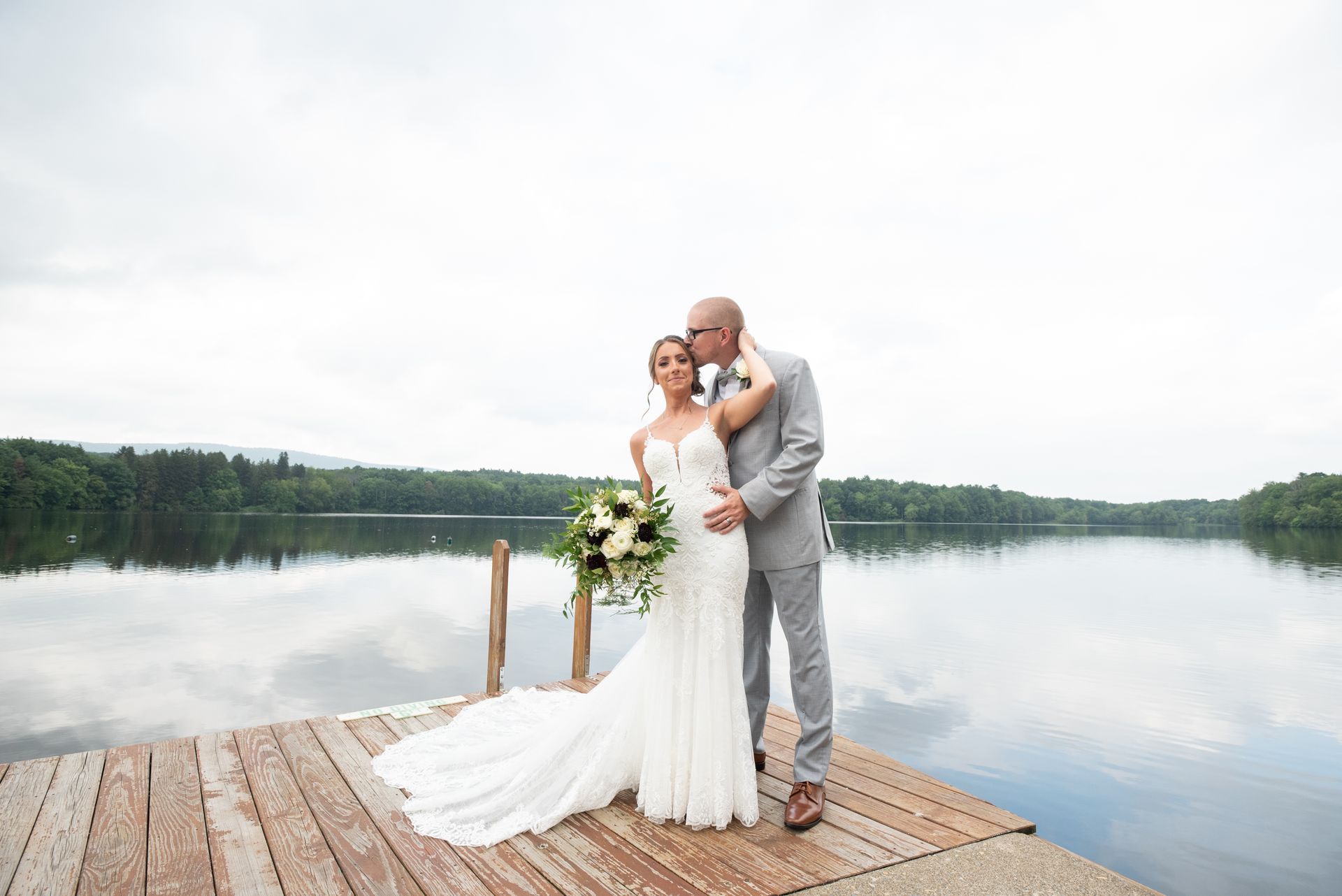 A bride and groom are posing for a picture on a dock next to a lake taken by Ever After Studio.