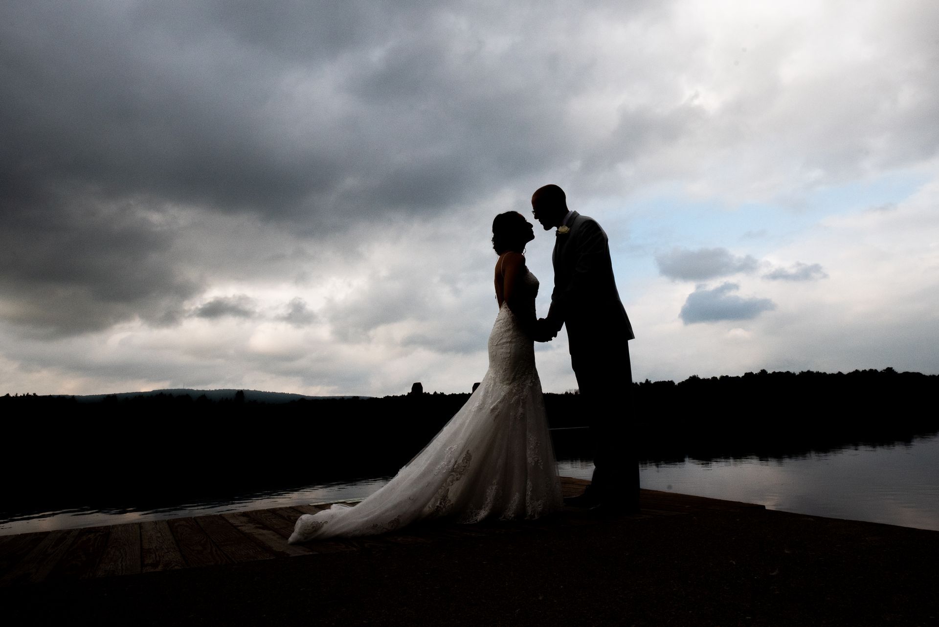 A bride and groom are standing next to each other on a dock holding hands taken by Ever After Studio.