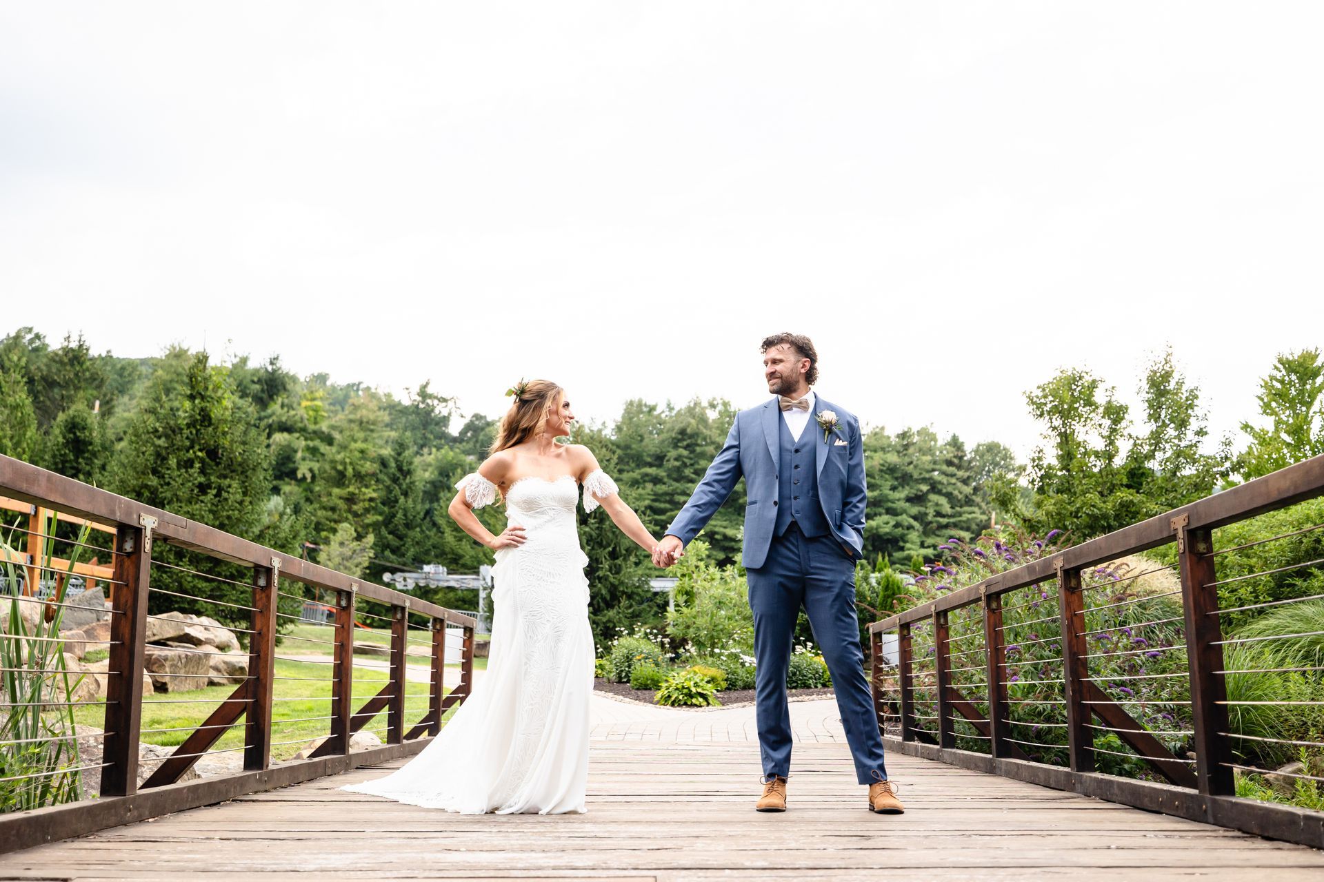 A bride and groom are standing on a wooden bridge holding hands taken by Ever After Studio.