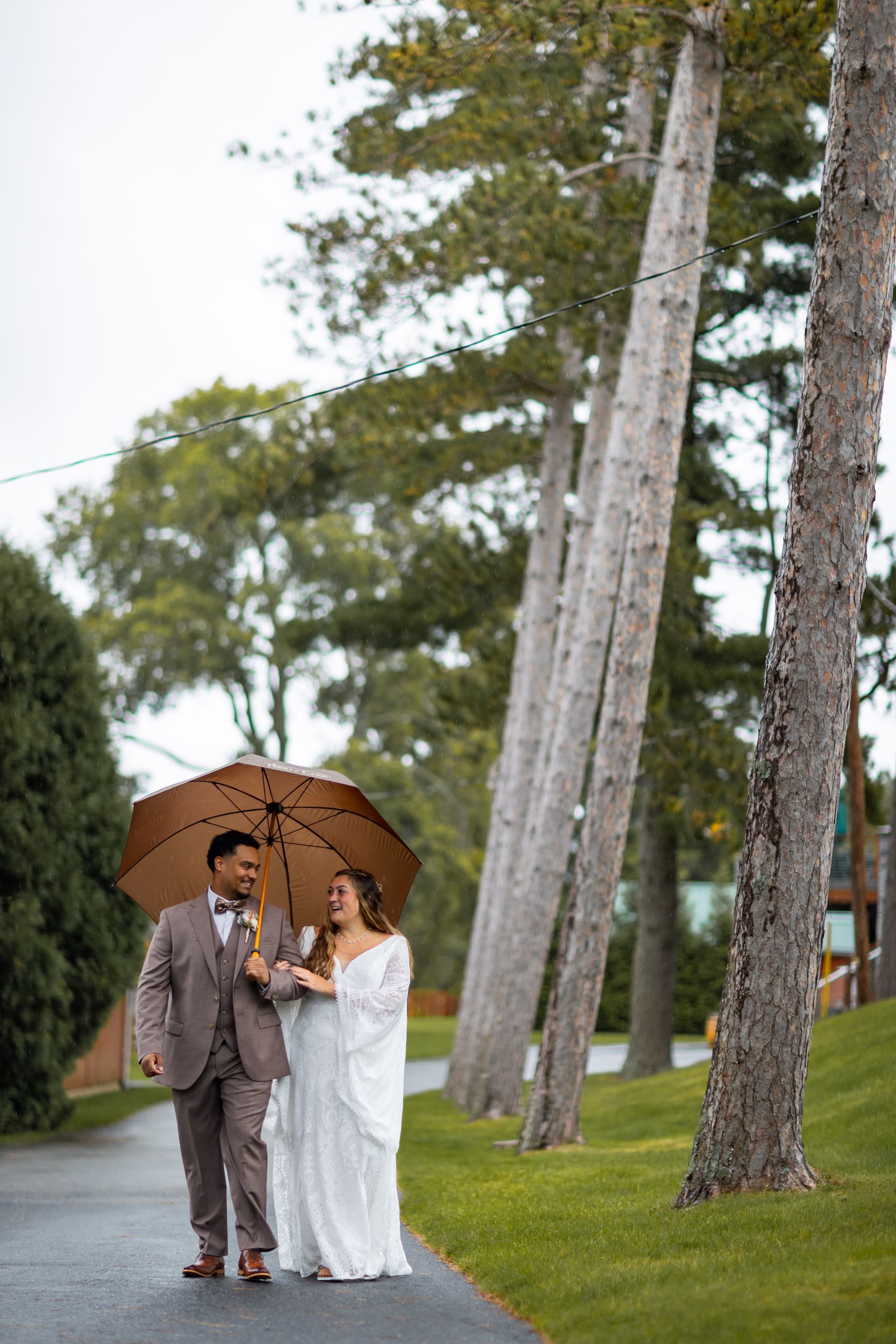 A bride and groom are walking under an umbrella in the rain taken by Ever After Studio.
