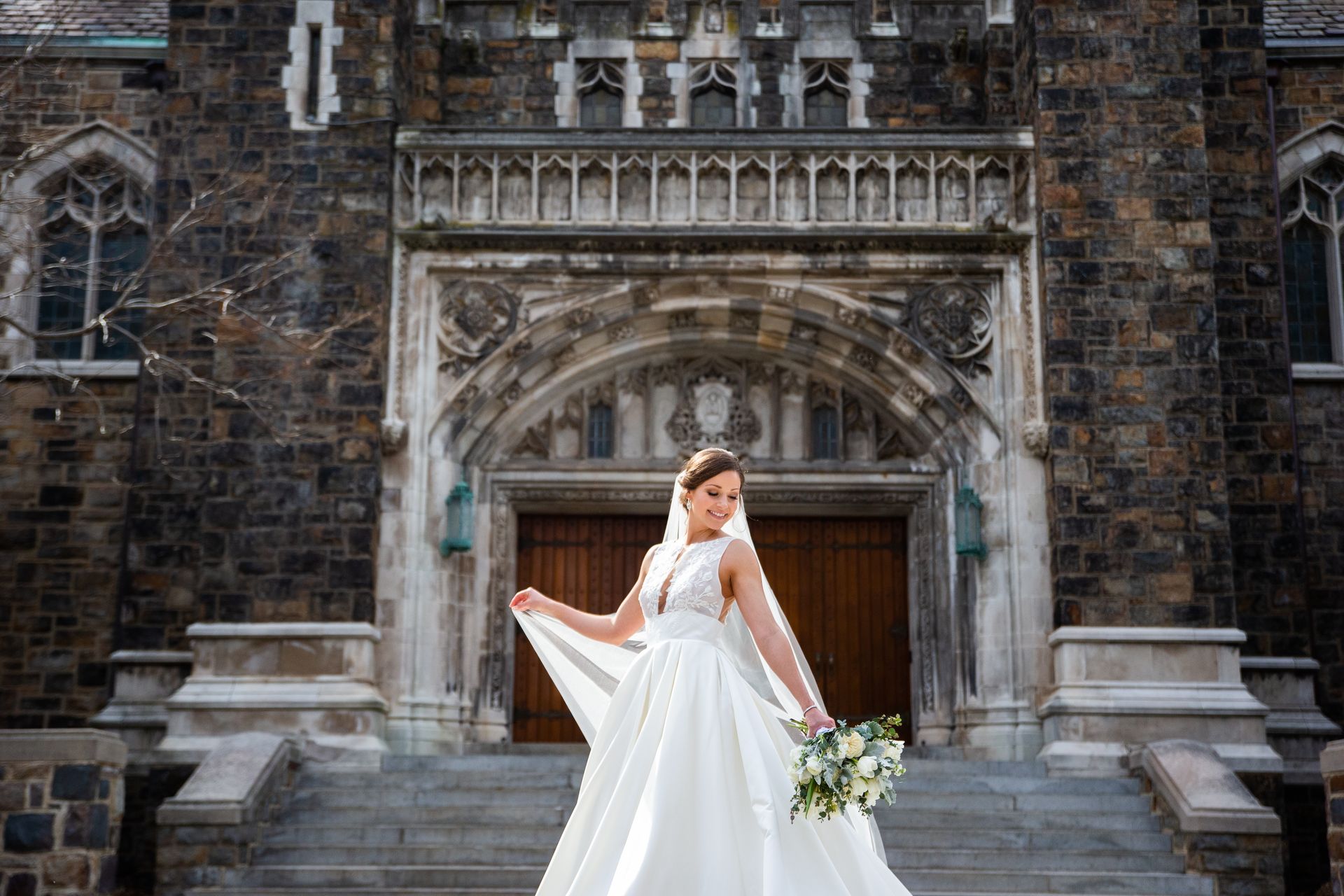 A bride in a wedding dress and veil is standing in front of a church taken by Ever After Studio.