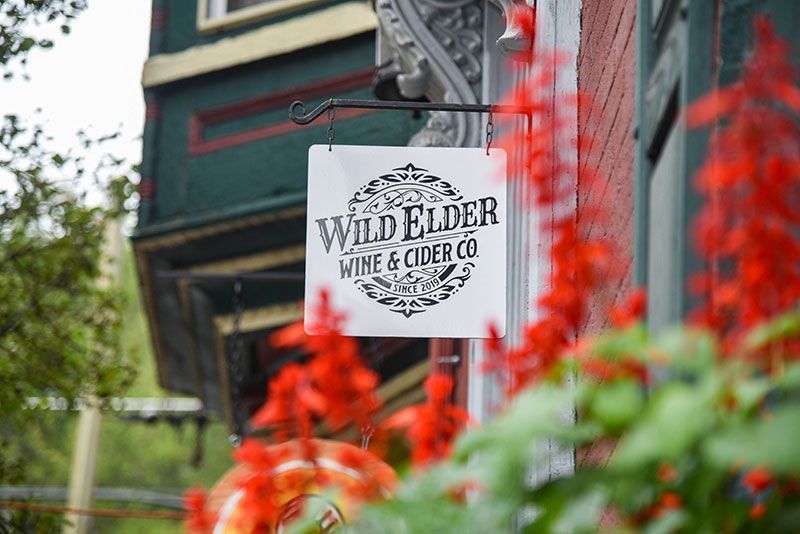 A sign for wild elder wine and cider co. hangs on the side of a building.