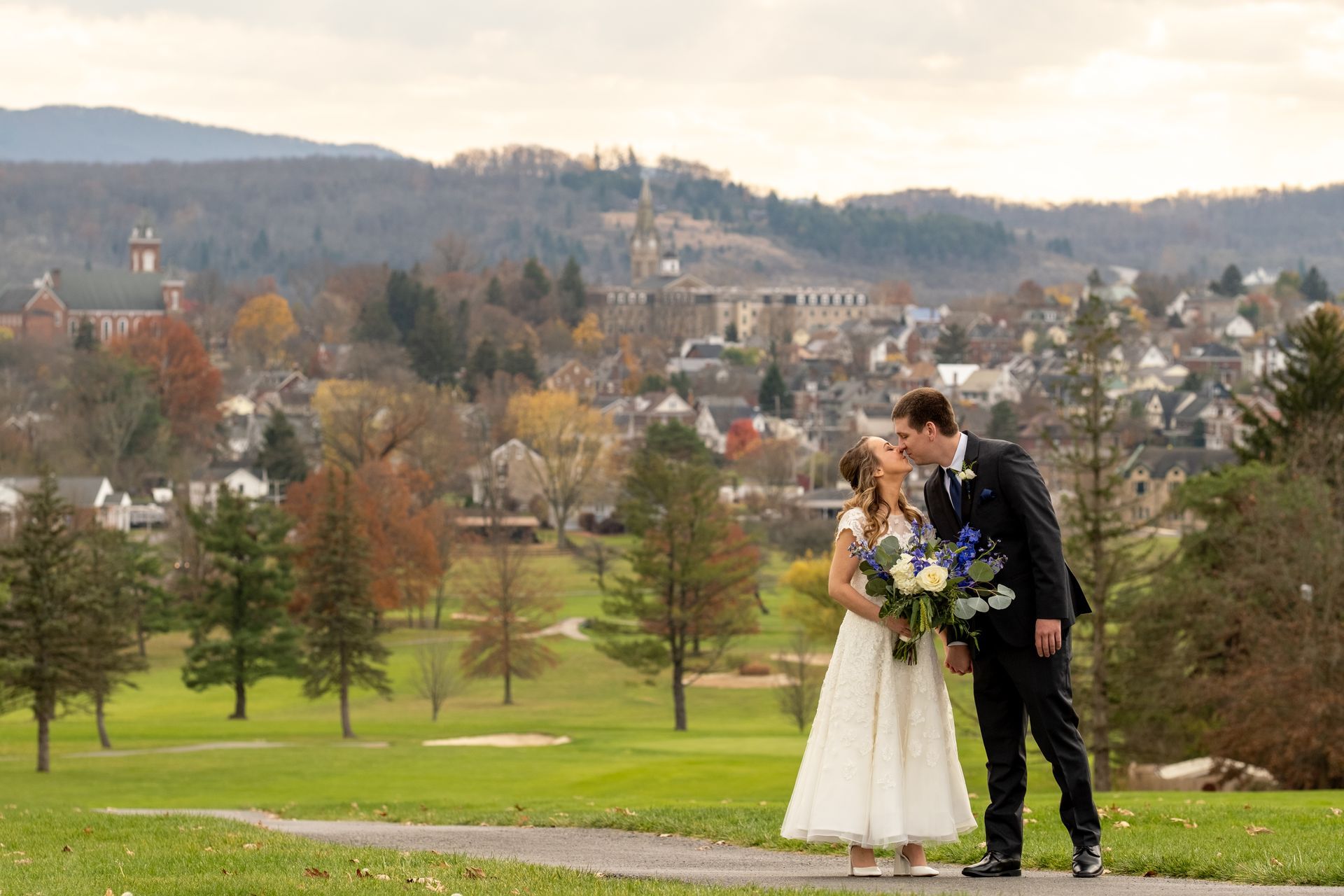 A bride and groom are kissing on a path in a park taken by Ever After Studio.