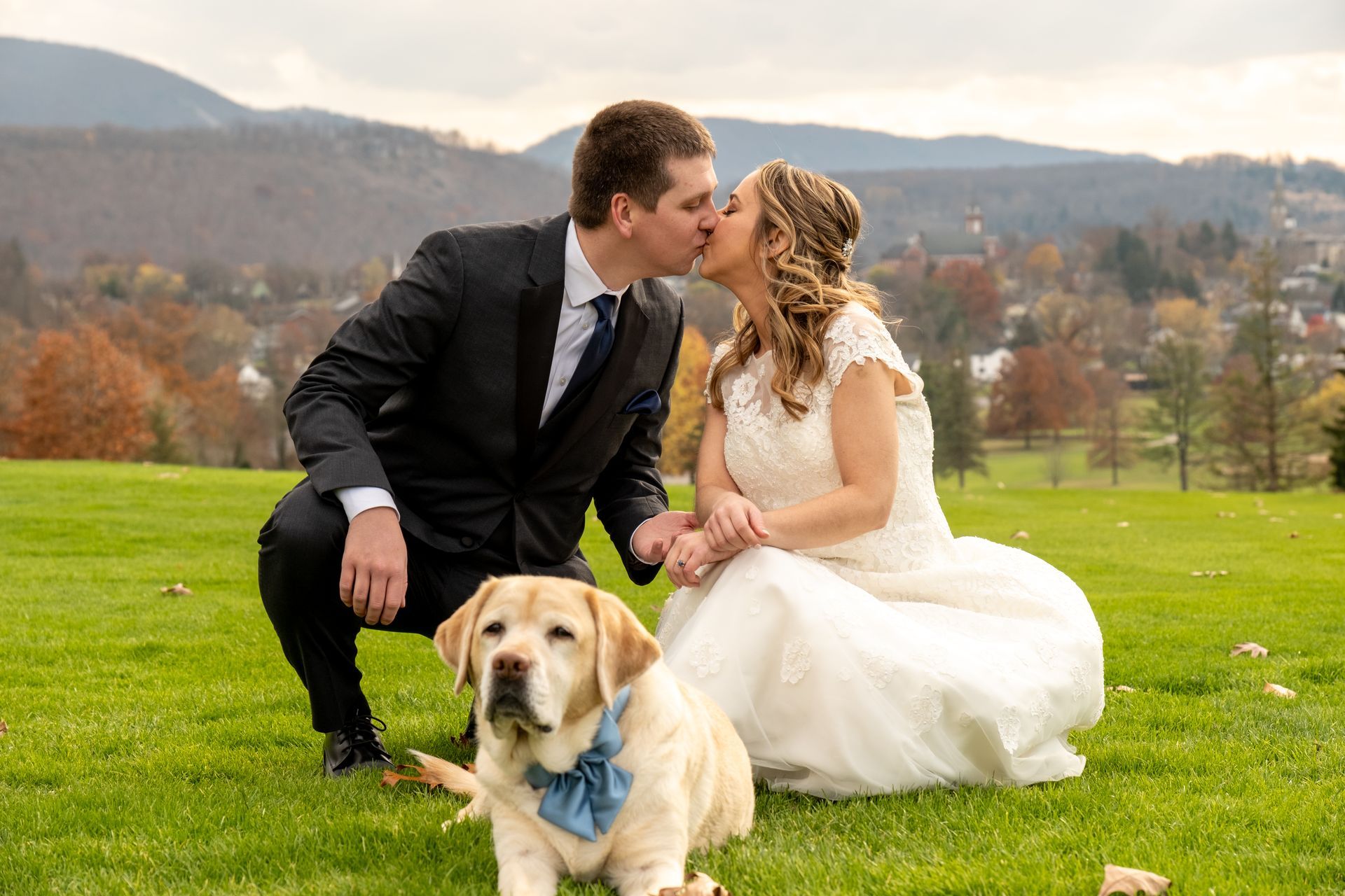 A bride and groom kissing next to a dog in a field taken by Ever After Studio.