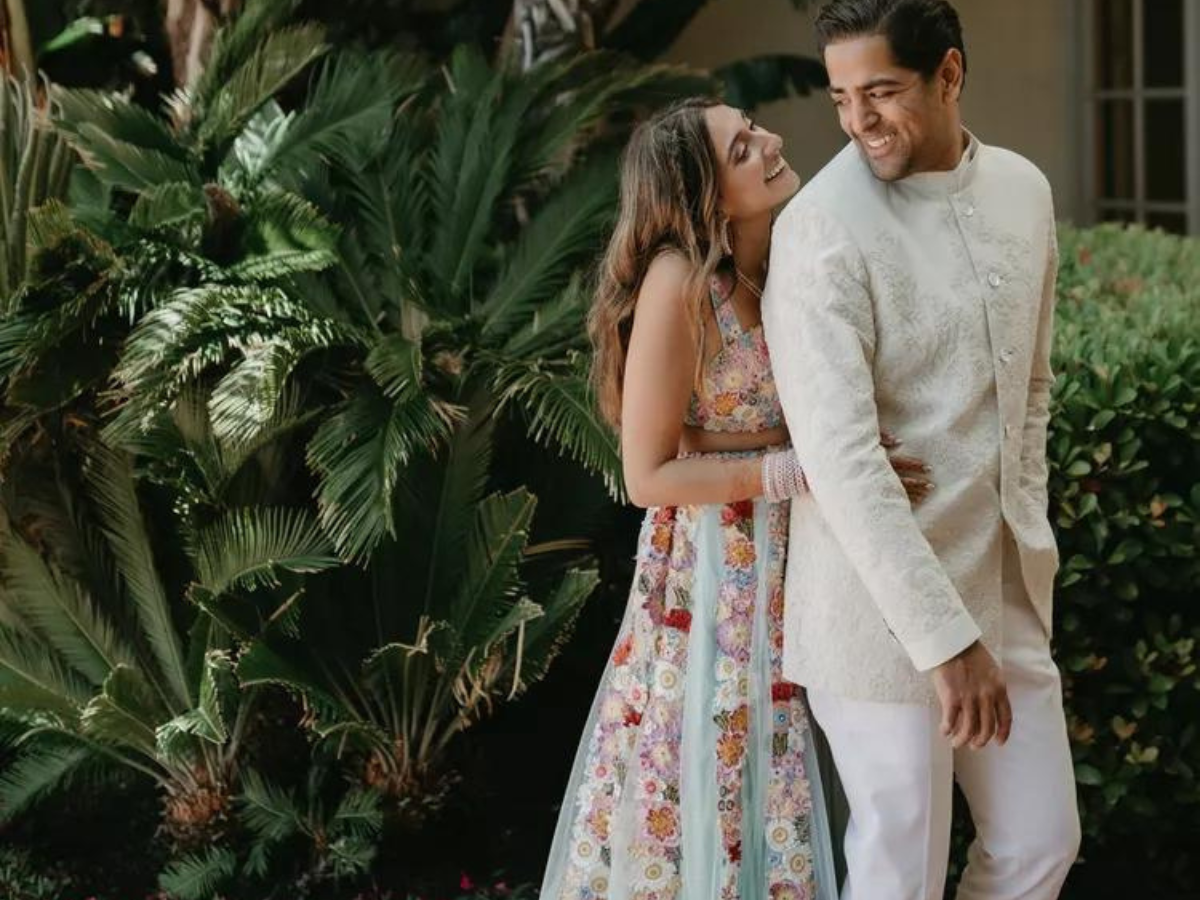 A man and a woman are standing next to each other in front of a palm tree in engagement outfits.