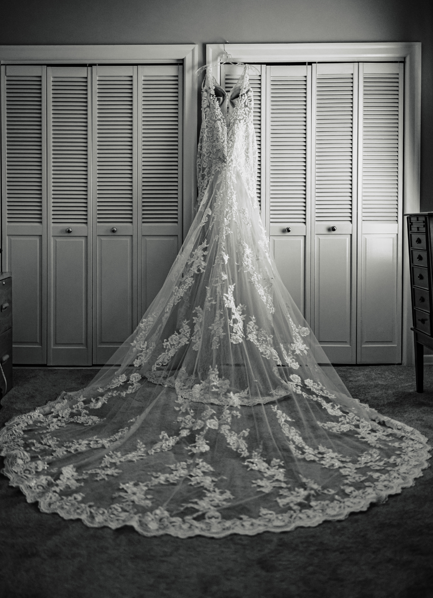 A black and white photo of a wedding dress hanging in a closet taken by Ever After Studios.