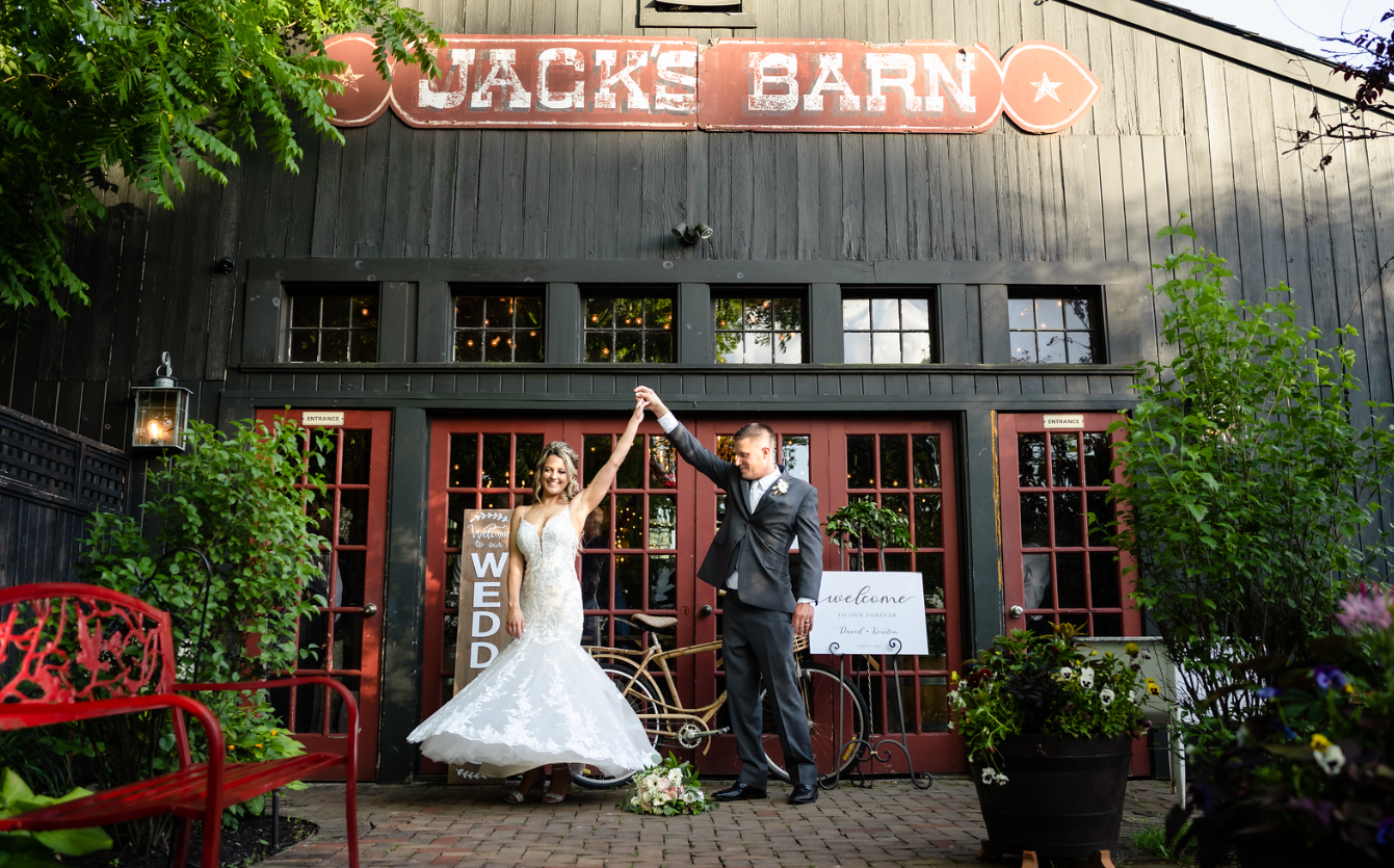 A bride and groom are posing for a picture in front of jack 's barn.